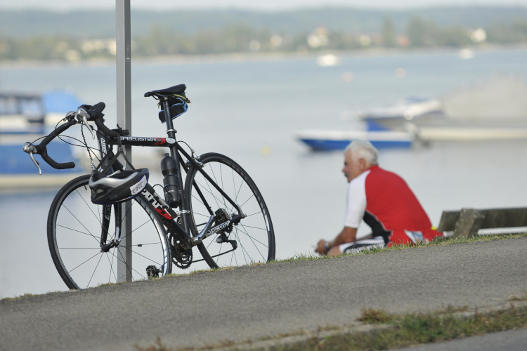 Mann sitzt auf Bank am See mit Rennrad